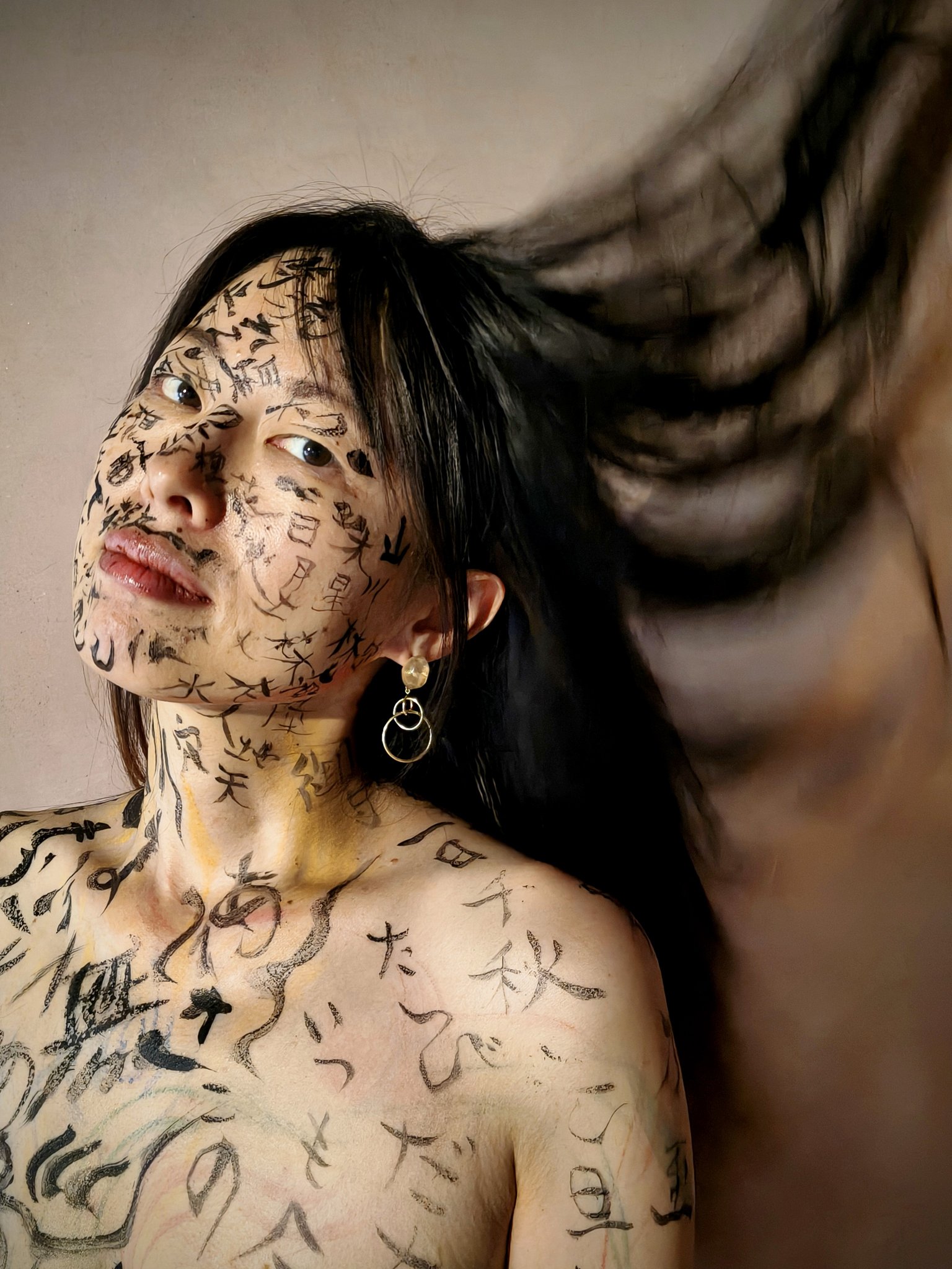 顔と胸に黒い書を描かれたタケダムツミ — 髪が大きく流れ、上を向く視線のクローズアップ